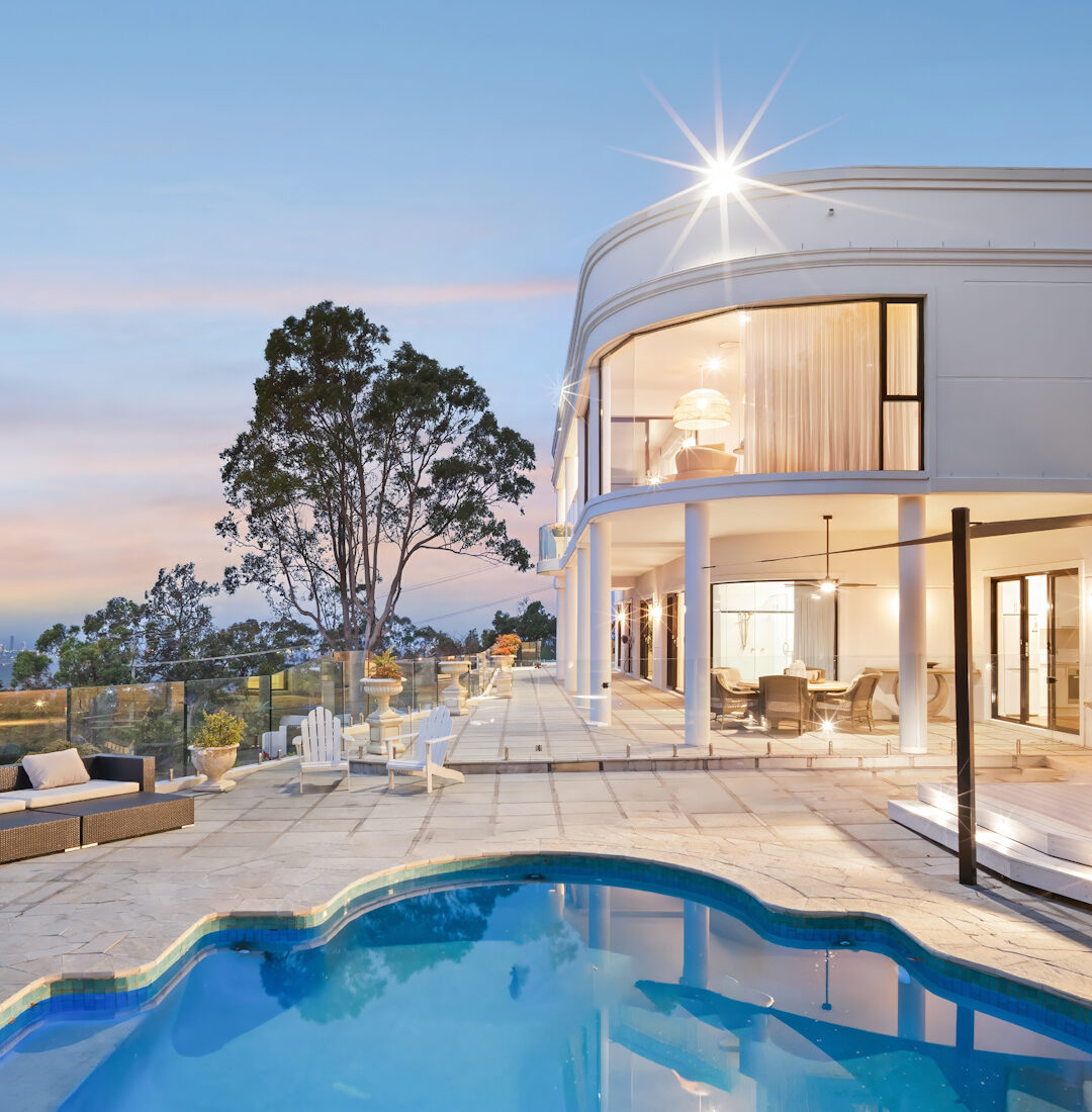 Gold Coast real estate photography of a luxury curved home exterior with resort-style pool, outdoor entertaining area, and elegant dusk lighting.