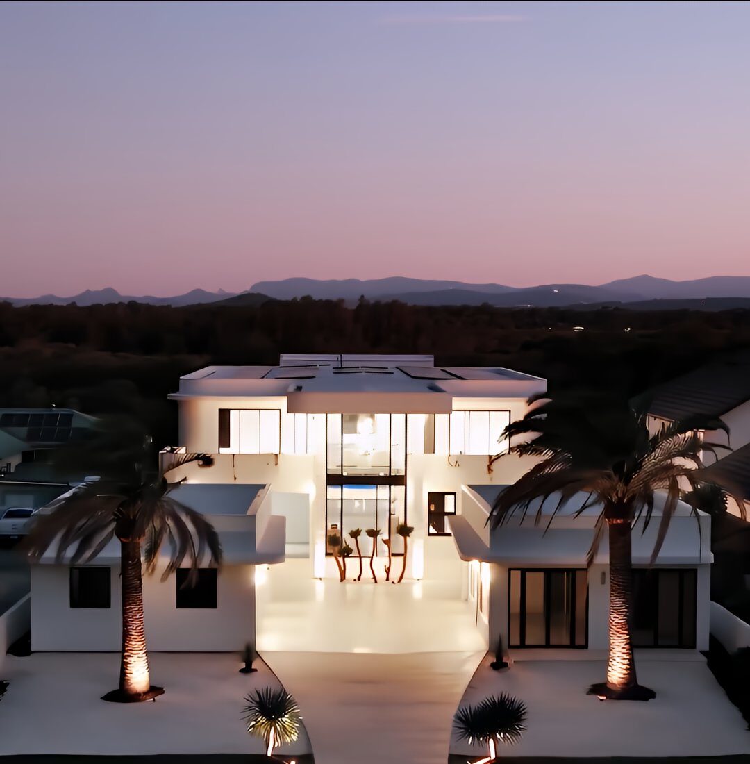 Gold Coast real estate videography of a luxury modern home at dusk with illuminated facade, palm-lined driveway, and cinematic exterior views.